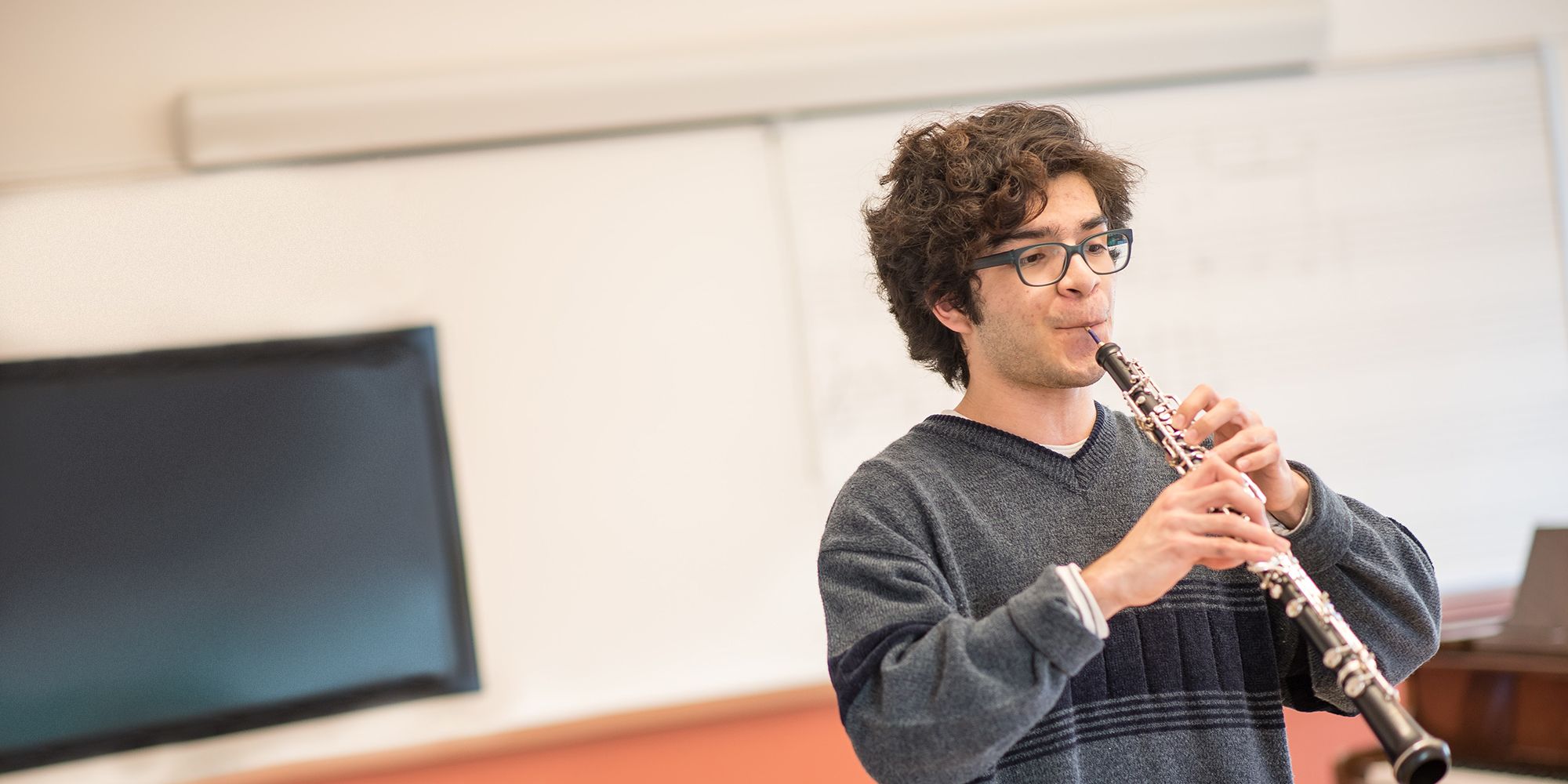 Oboe: a man in a grey sweater plays in the oboe in the front of a classroom