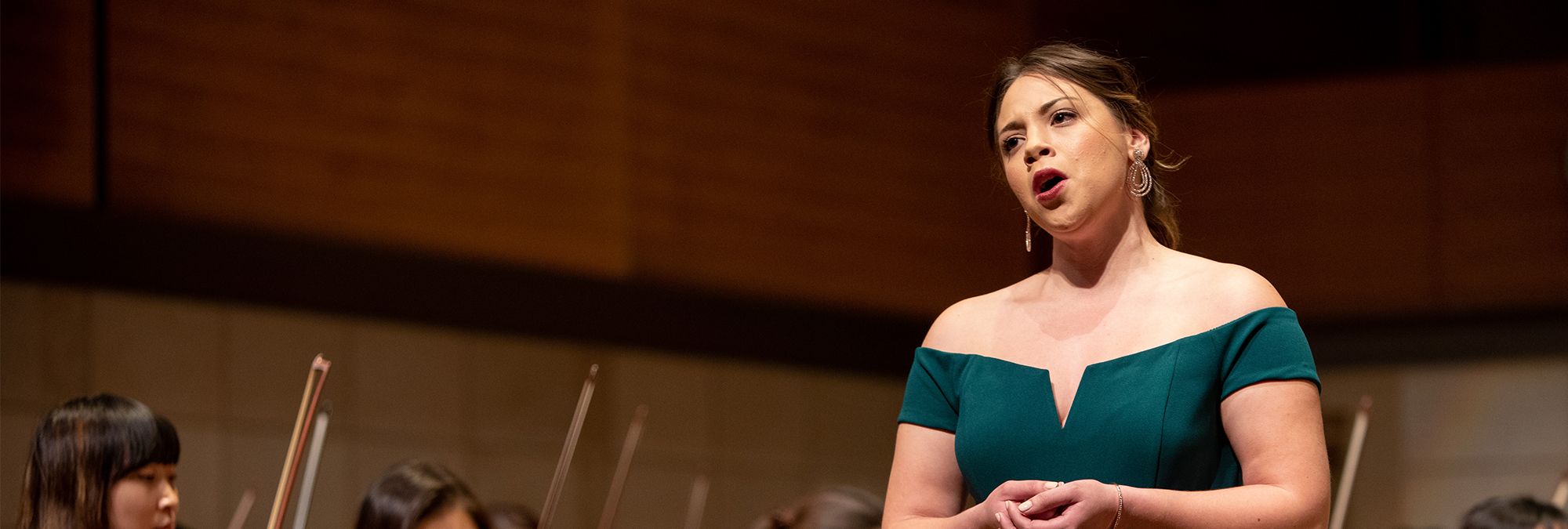 Voice: a woman in a teal dress sings on stage in front of an orchestra