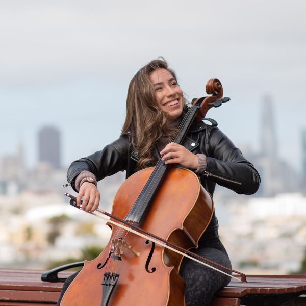 a cellist plays outside while smiling