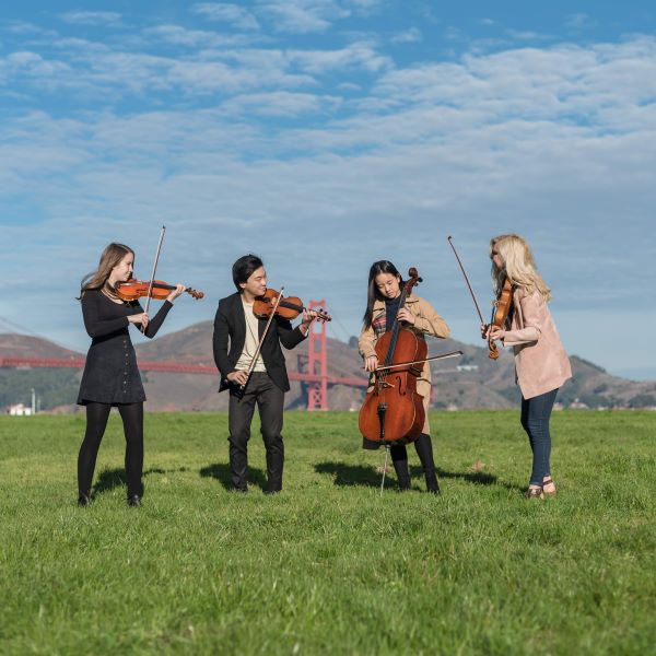 string quartet stands and laughs in a park with the golden gate in the background