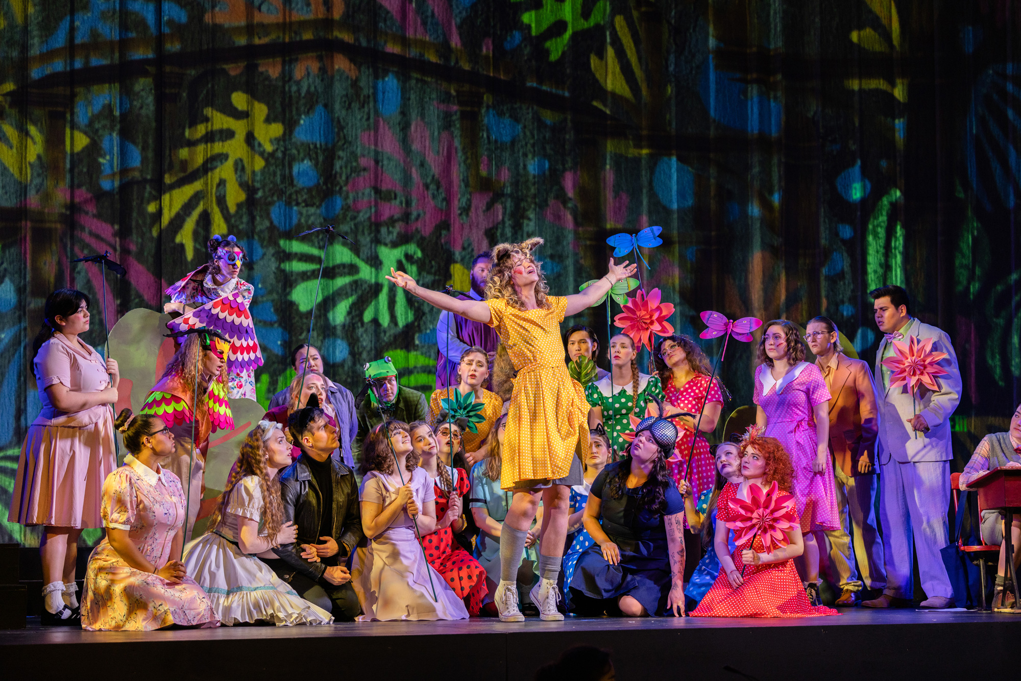 two dozen opera singers huddled around one main singer in colorful costumes