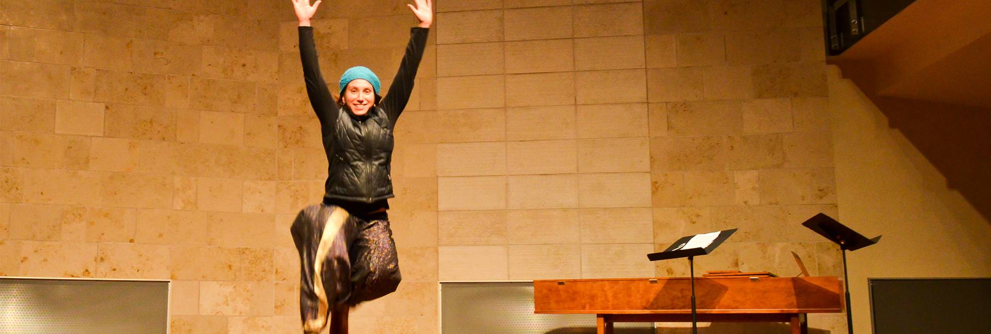 a person jumping with their hands up in the recital hall
