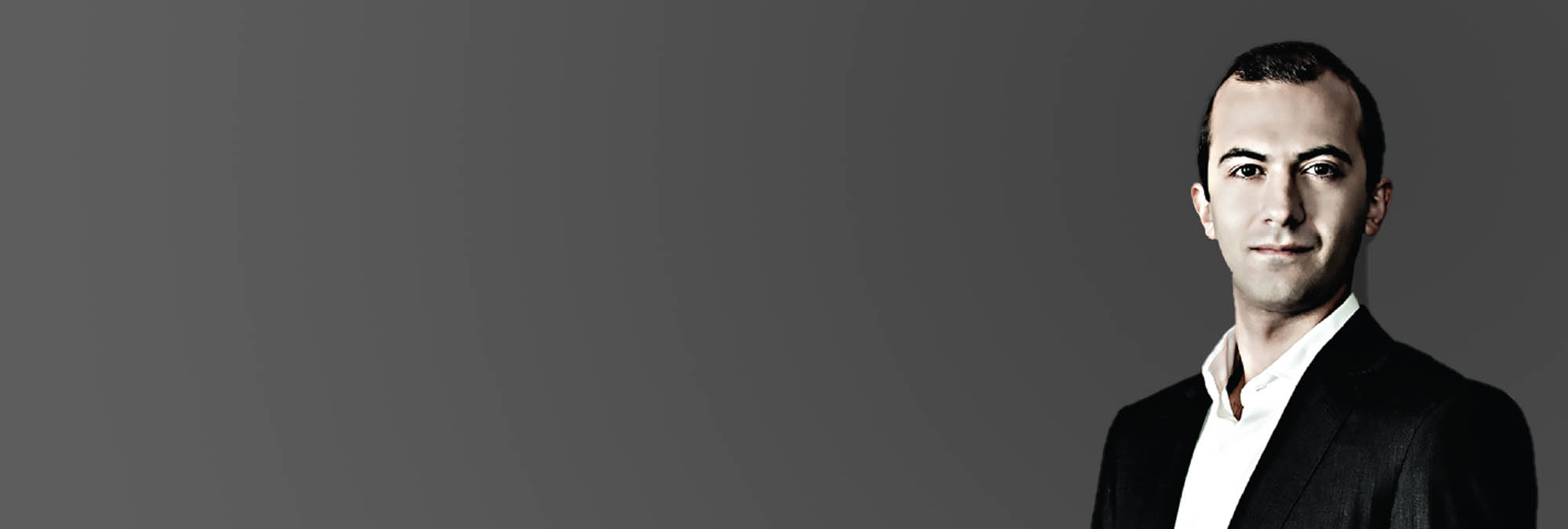 A headshot of a smirking male against a gray background