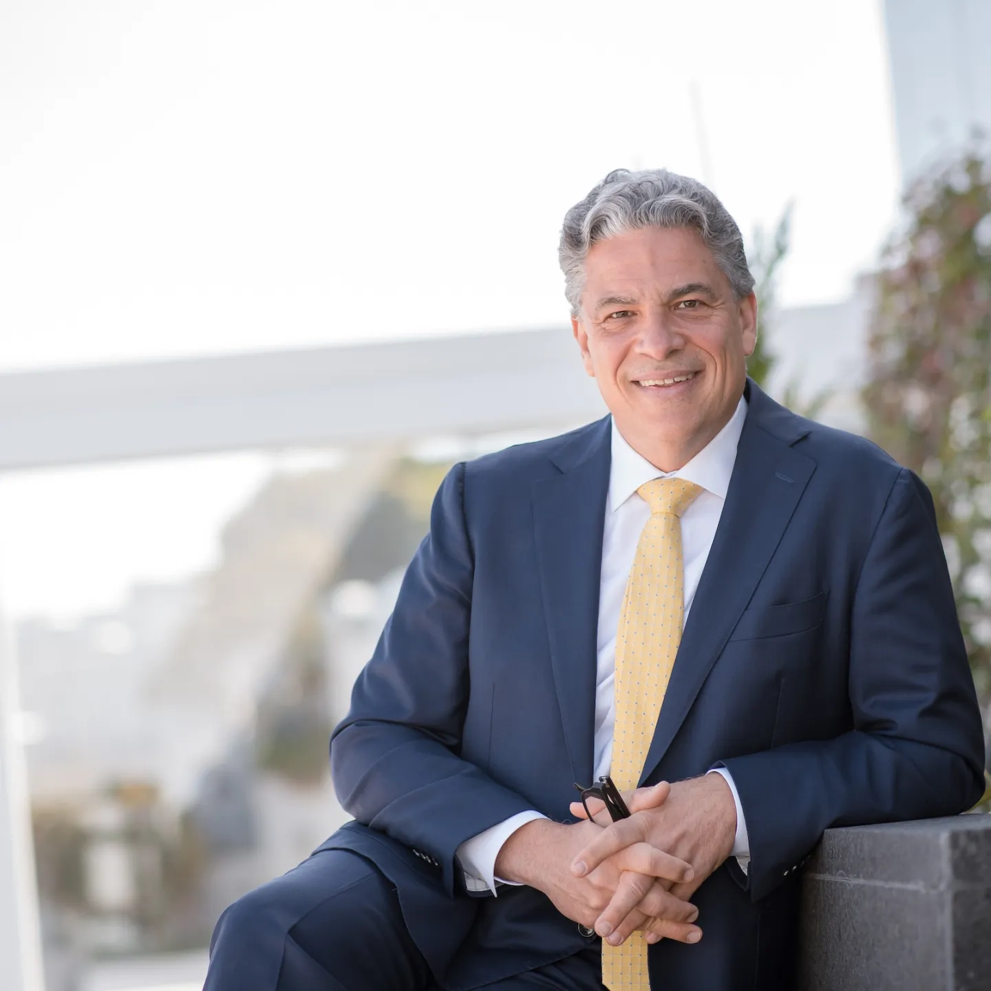 Portrait of David Stull, smiling while sitting outdoors and wearing a navy blue suit.
