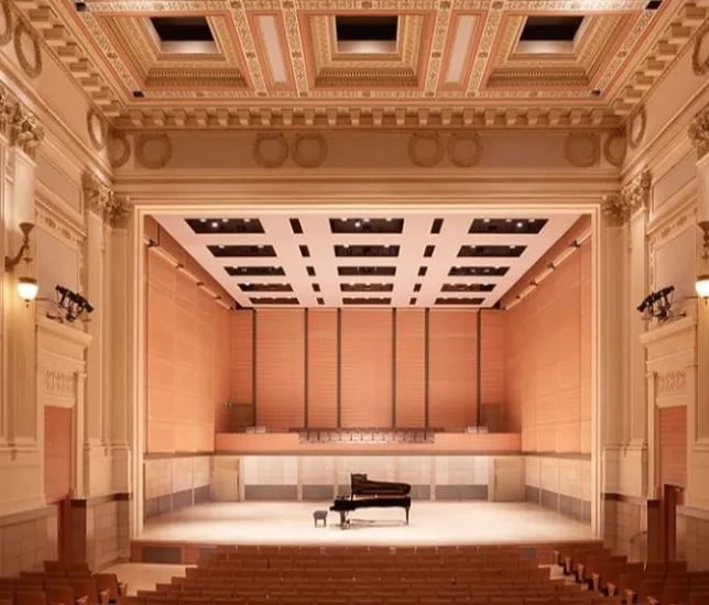a shot of an empty concert hall, brightly lit with a piano in the center of the stage