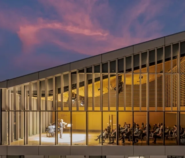 a drone photo of the top floor Osher recital hall during a recital. there is a sunset in teh background