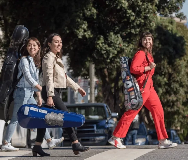 Three smiling students with instruments cross a San Francisco street