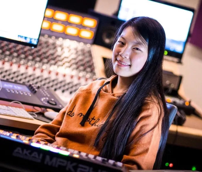 A female student surrounded by a number of computers and digital creation tools