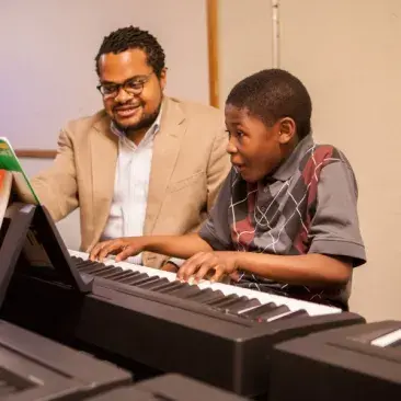 a student looks extremely excited while playing piano with a teacher