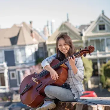 cellist holds her cello like a guitar with the painted ladies in the background