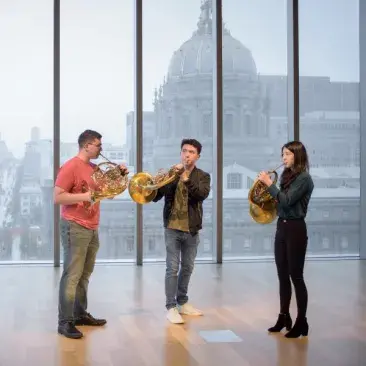 three horn players stand in front of city hall from the 11th floor of the bowes center