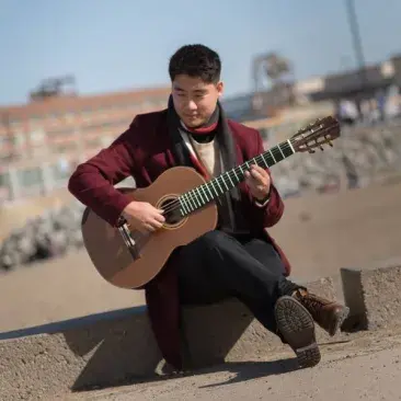 a guitarist plays sitting along the sea wall, with the beach behind him