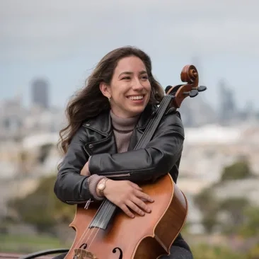 cellist sitting in front of SF skyline