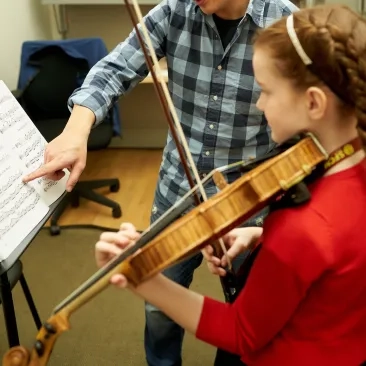 A young music student works with a teacher. 