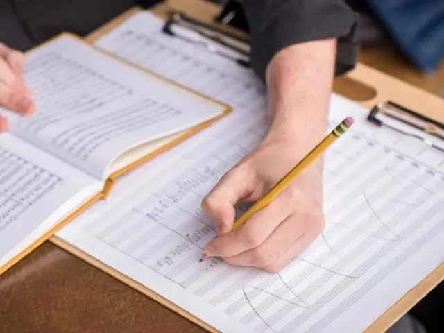 a student sits at a desk writing notes on a score