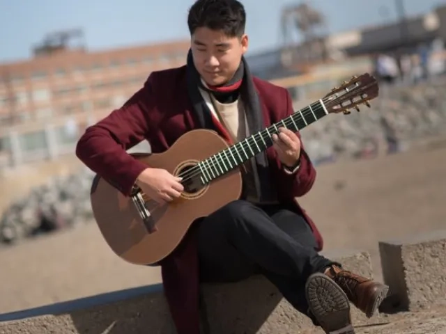 a guitarist plays sitting along the sea wall, with the beach behind him