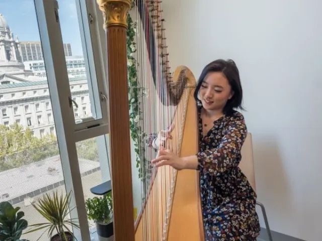 a harpist practices in her dorm with city hall in the background