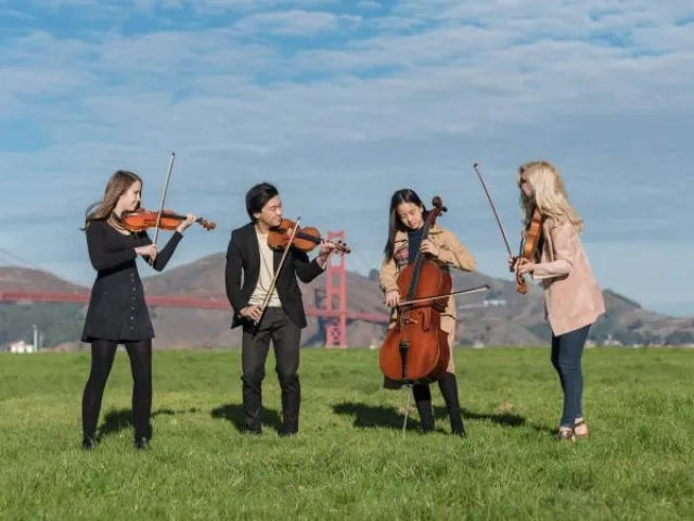 string quartet stands and laughs in a park with the golden gate in the background