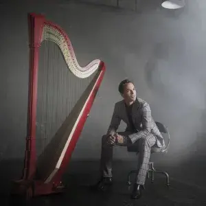 Emmanuel Ceysson headshot with harp in a smokey room