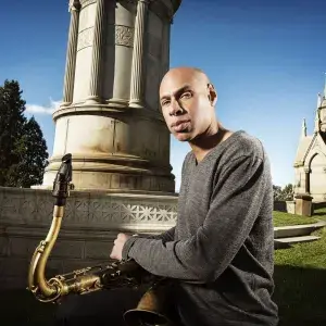 Joshua Redman headshot outdoors while holding saxophone