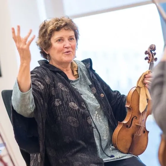 Elizabeth Blumenstock Headshot with a violin, gesturing to students