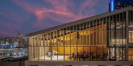 a drone photo of the top floor Osher recital hall during a recital. there is a sunset in teh background