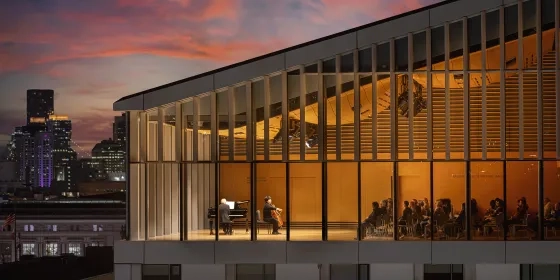 Bowes Center from the outside at dusk, with a performance visible through the windows.