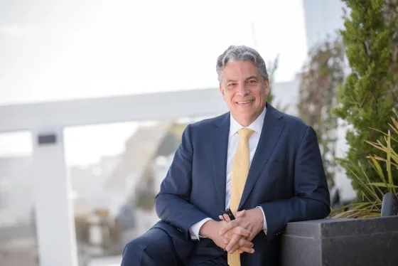 Portrait of David Stull, smiling while sitting outdoors and wearing a navy blue suit.