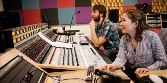 Two students working with recording studio equipment inside a colorful studio.