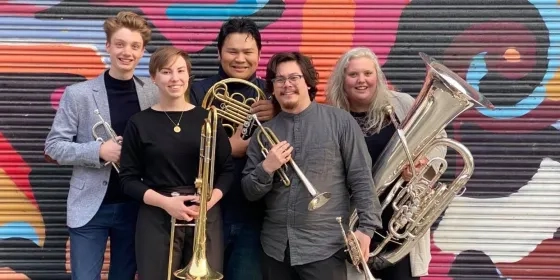 The Barbary Coast Brass Quintet stand with instruments in front of colorful wall