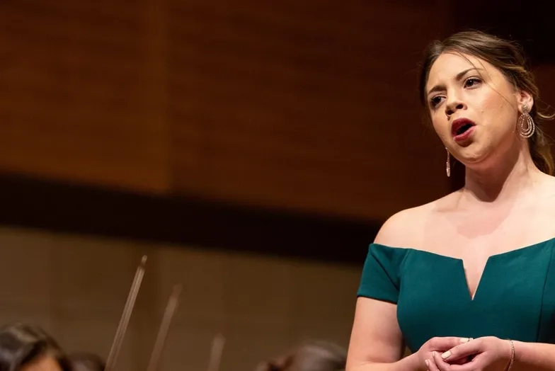 Voice: a woman in a teal dress sings on stage in front of an orchestra