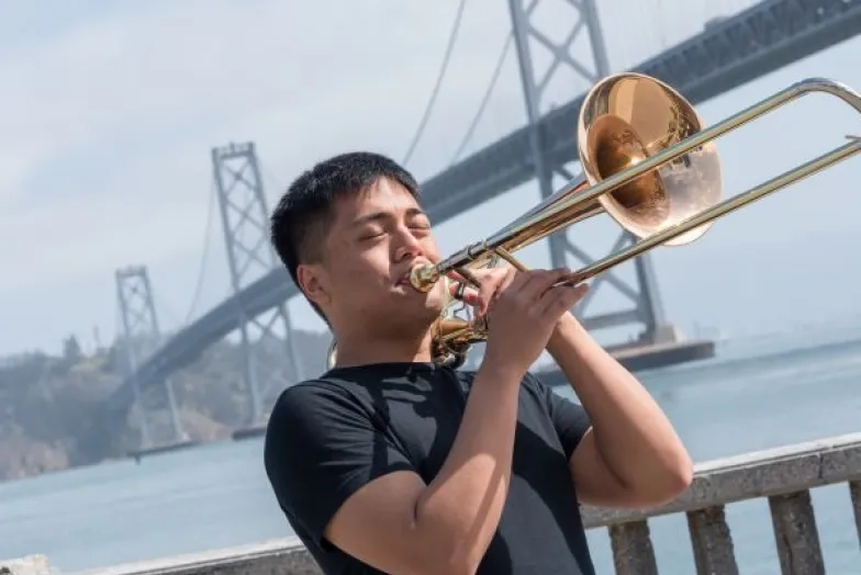 1-1-bass-trombone-outside.jpg a student plays trombone in front of the bay bridge