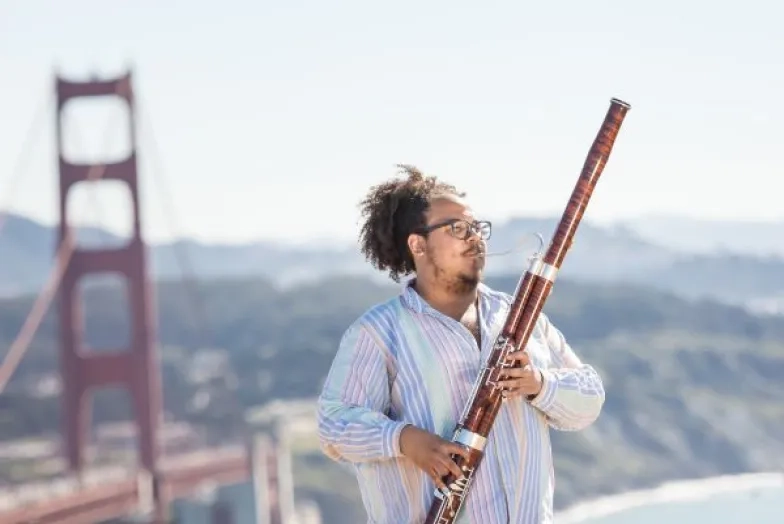 a student plays bassoon outside with the golden gate bridge in the background