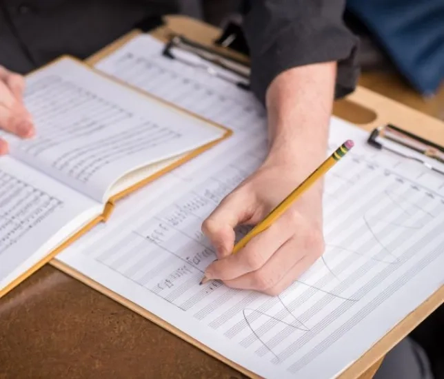 a student sits at a desk writing notes on a score