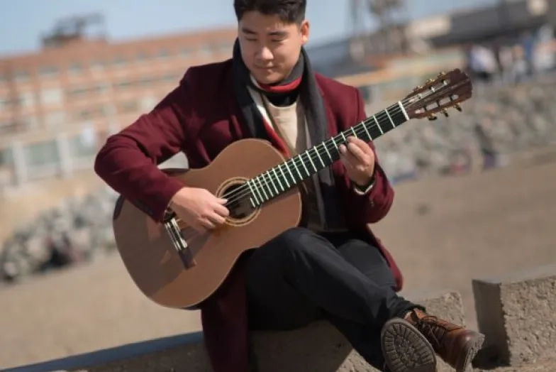 a guitarist plays sitting along the sea wall, with the beach behind him