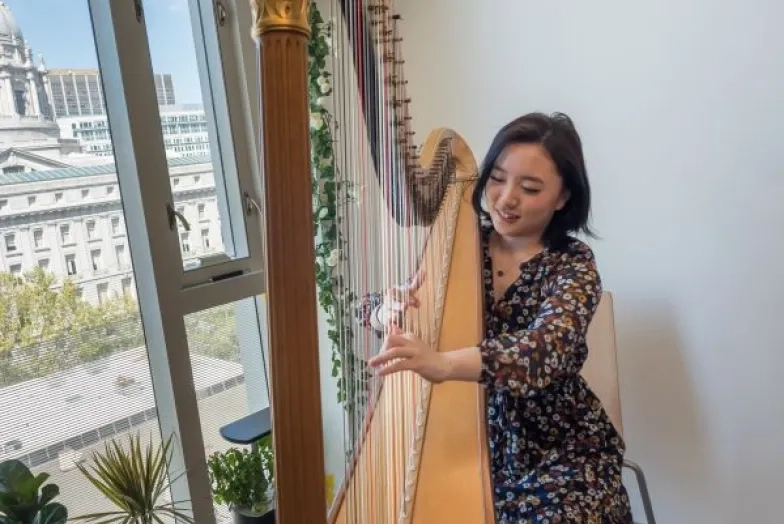 a harpist practices in her dorm with city hall in the background