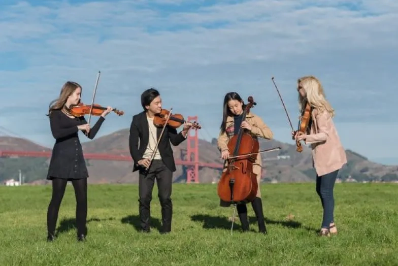 string quartet stands and laughs in a park with the golden gate in the background