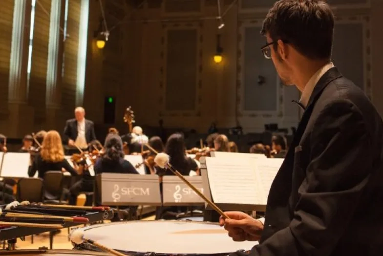 a timpani player watches the conductor in a dress rehearsal