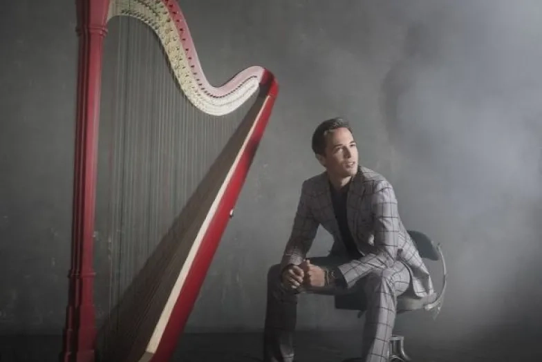 Emmanuel Ceysson headshot with harp in a smokey room