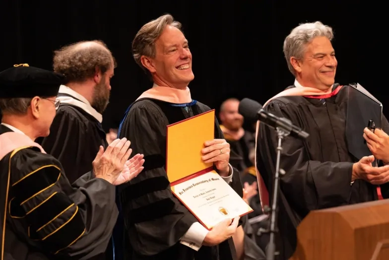 Jake Heggie holds a diploma with dean wright and david stull