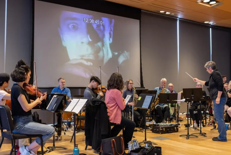 Students rehearse with a movie backdrop playing behind them