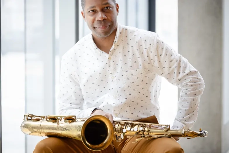 Jason Hainsworth with his saxophone, sitting in a chair