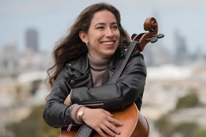 cellist sitting in front of SF skyline