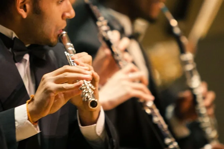A performer wearing a tuxedo plays the flue in an orchestra