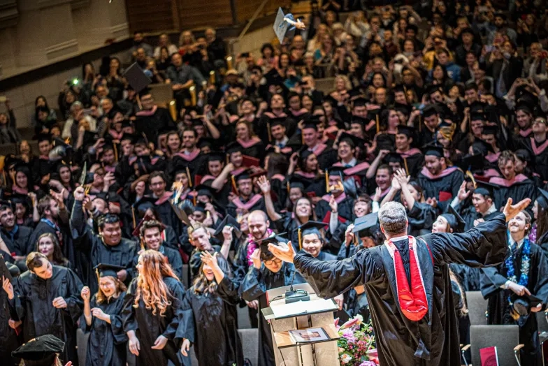 The Full Student Body smiling before throwing their caps at commencement