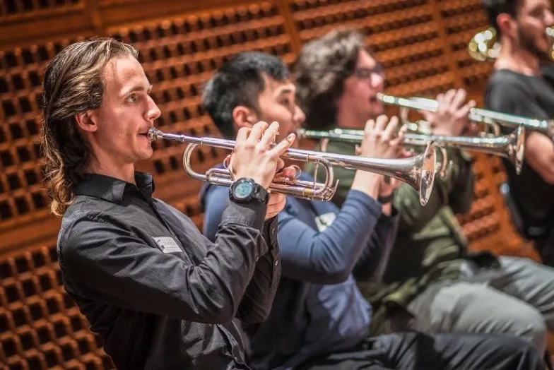 A trumpet player in focus against a backdrop of various other out of focus trumpet players