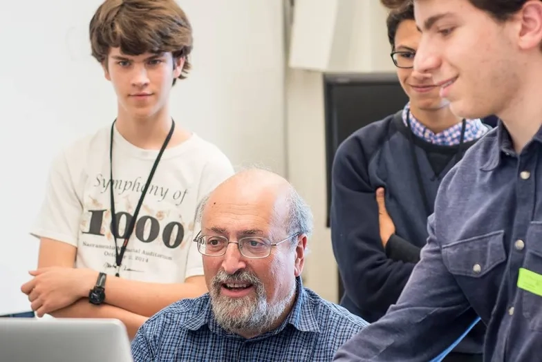 Three students looking over a teacher's shoulder at the computer