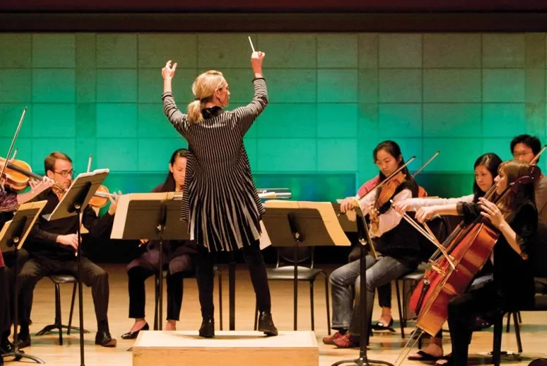 conductor conducting new music ensemble with dramatic hall lighting