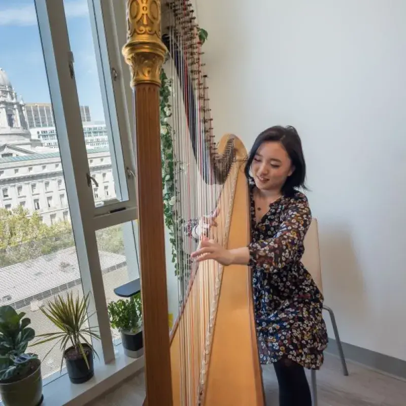 a harpist practices in her dorm with city hall in the background