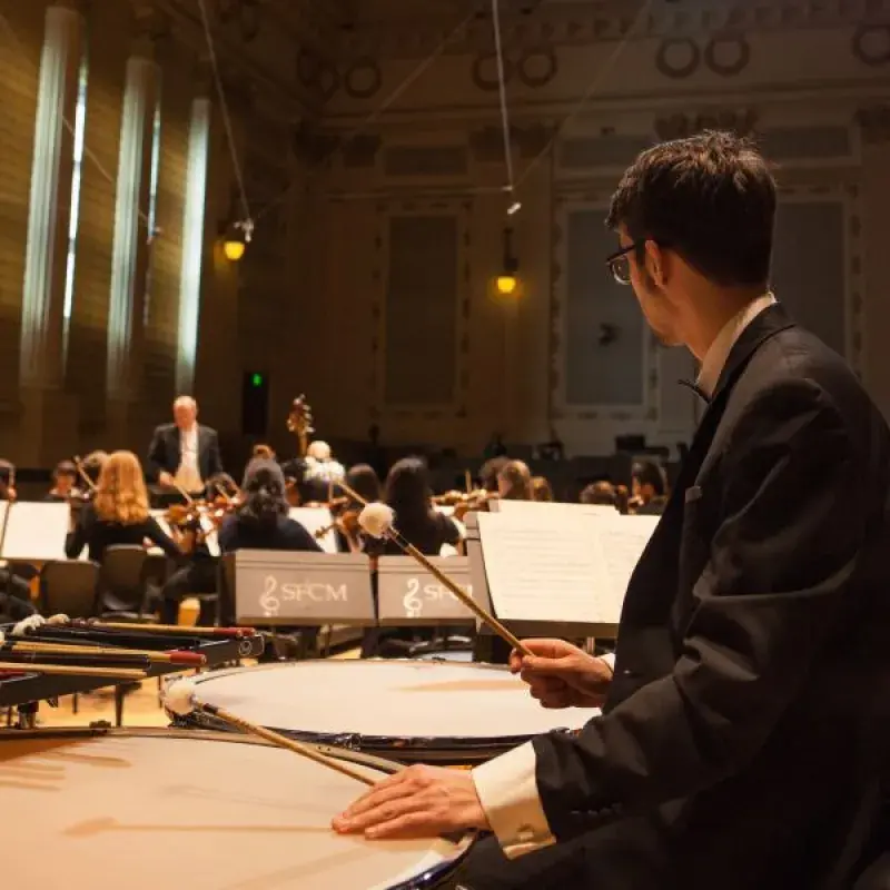 a timpani player watches the conductor in a dress rehearsal